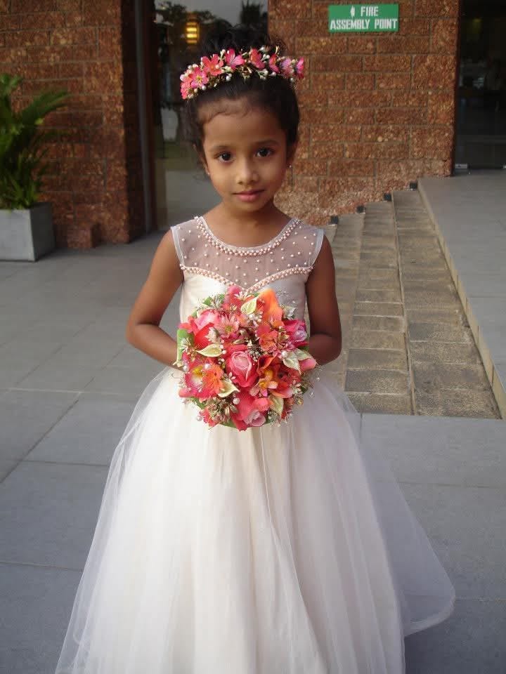 Chuutimanikaa as a little girl in a white dress holding flowers